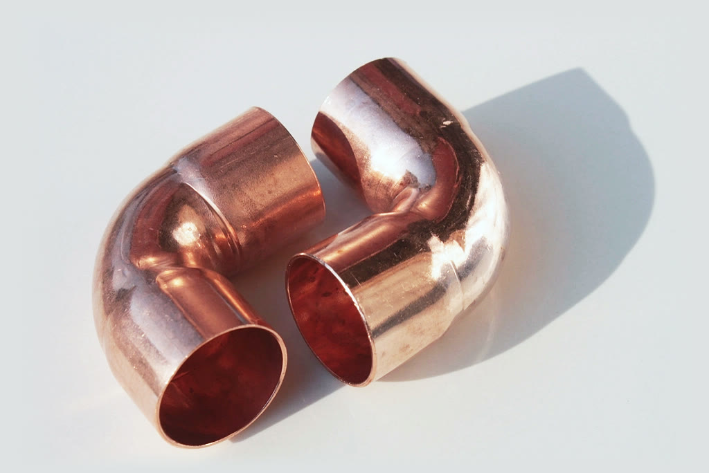 Two copper elbow fittings resting on a pale gray surface