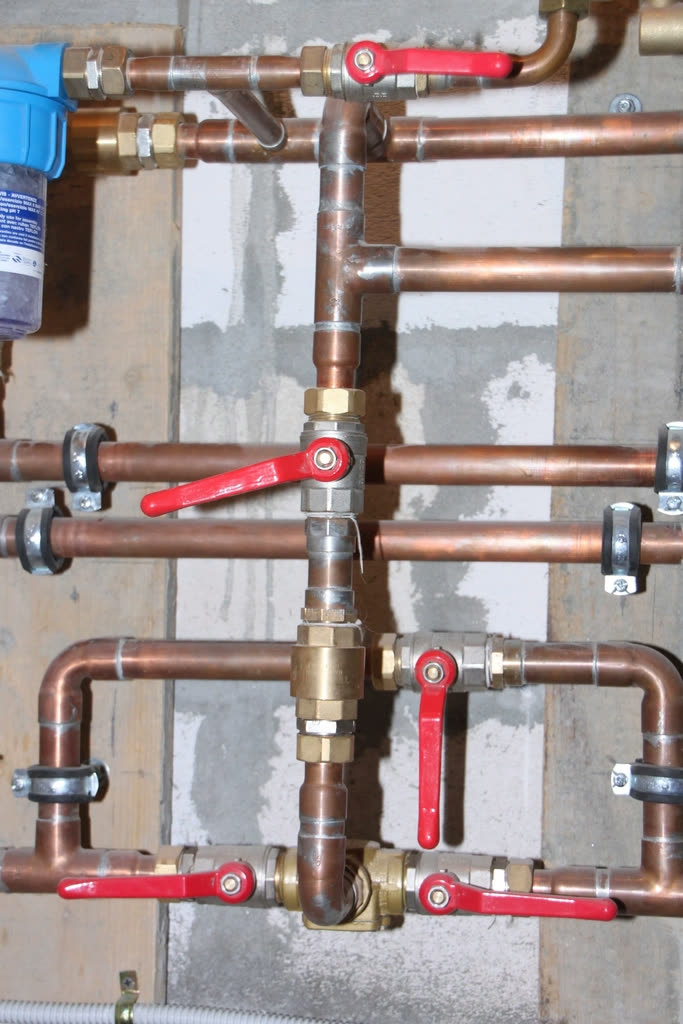 Copper water lines on a wall, each fitted with a red lever shutoff valve